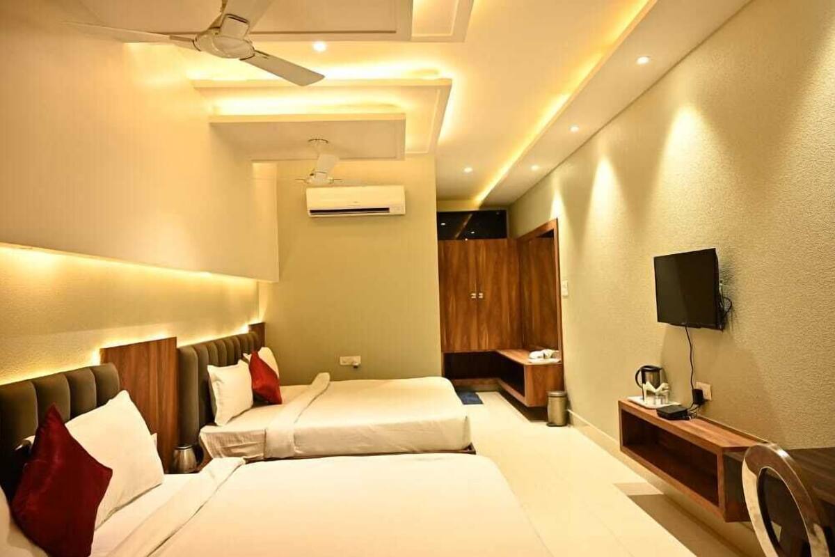 Une chambre d’hôtel avec deux lits, un ventilateur de plafond, un appareil de climatisation, une télévision et un bureau en bois.