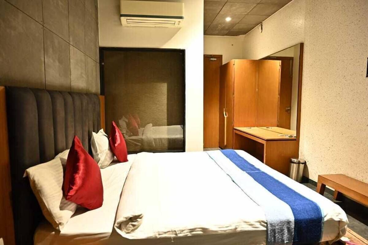 Une chambre d’hôtel avec un lit, une armoire en bois, un banc et un miroir.