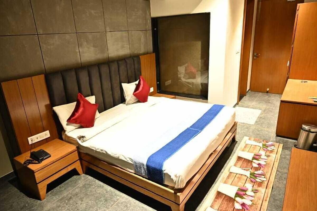 Une chambre d’hôtel avec un grand lit, une table de chevet en bois, un bureau avec une poubelle et une fenêtre donnant sur un beau paysage.