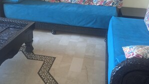 Una stanza con un divano blu, cuscini decorati, un tappeto a motivi e un tavolino ornamentale.