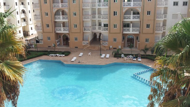 Un hotel con piscina, numerosi balconi e palme.