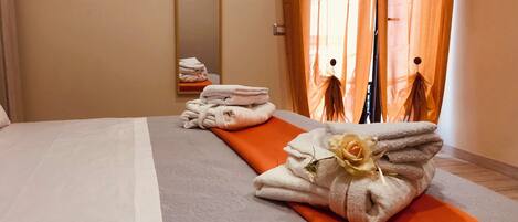 A hotel room with a neatly made bed, a stack of towels, and a mirror on the wall.