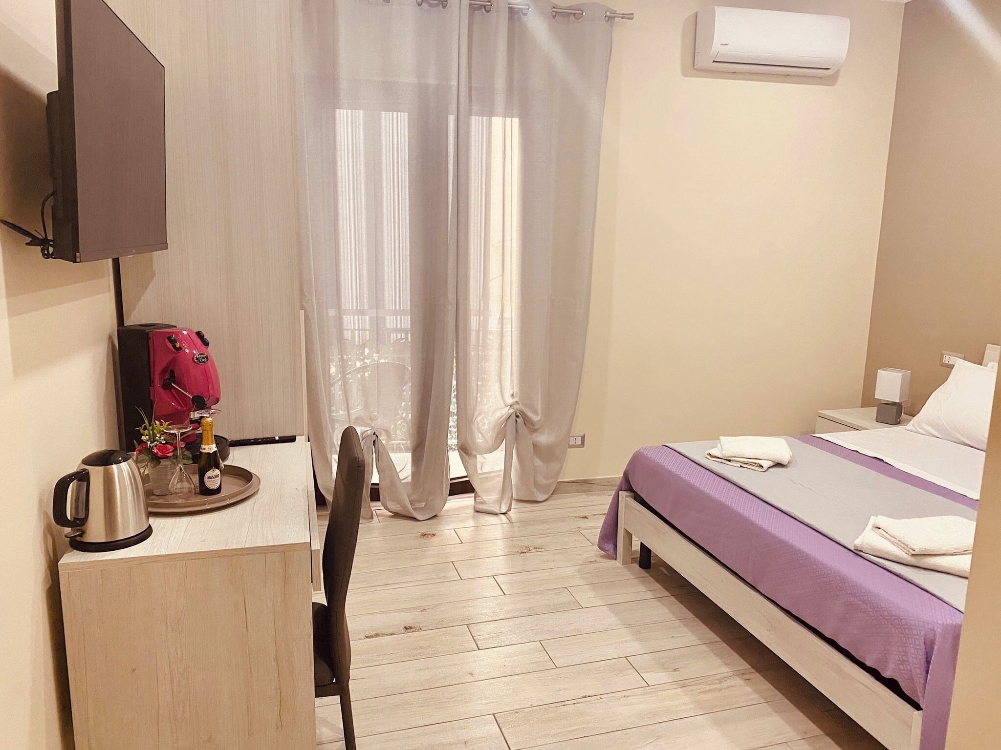 Una camera d'albergo con un letto, una scrivania con una macchina del caffè, una sedia e un televisore montato a parete.
