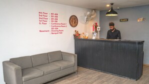 Un área de recepción con un sofá gris, un mostrador negro, un reloj y un cartel que indica la recepción.