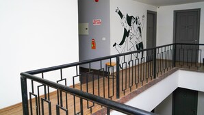 Interior de varios niveles con barandilla de metal negro, detector de incendios en la pared y puerta con placa de número.