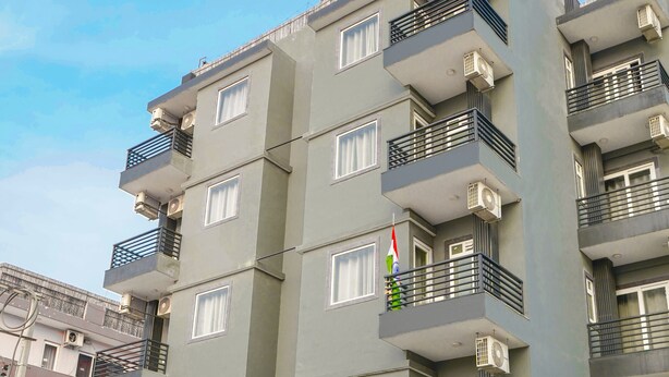 Un edificio residencial de varios pisos con balcones, unidades de aire acondicionado y una entrada protegida por una reja.