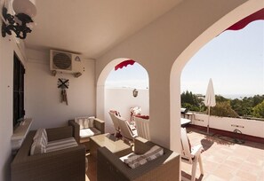 A covered outdoor seating area with wicker furniture, a white air conditioning unit, and a view of the sea.