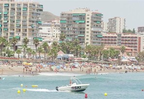 A coastal scene with a boat labeled 'SKI' on the water, a beach with umbrellas, and high-rise buildings in the background.