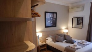 A hotel room with a bed, bedside lamps, a wooden nightstand, and a wall-mounted air conditioner. - Hôtel Miramar Cap d'Antibes (Antibes)