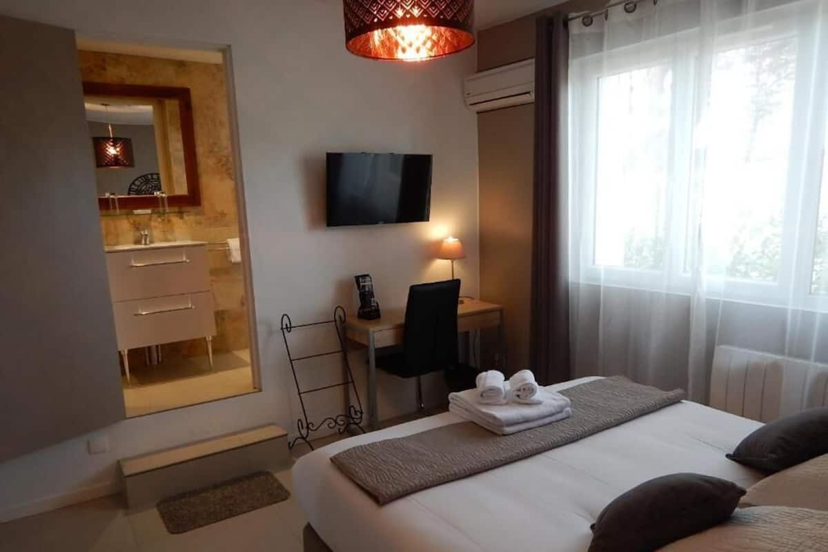 Ett hotellrum med en säng, ett skrivbord med en stol, en tv och ett badrum som syns genom en öppen dörr.