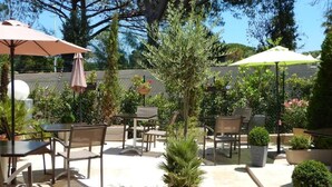 An outdoor patio area with tables and chairs, potted plants, and umbrellas. - Hôtel Miramar Cap d'Antibes (Antibes)