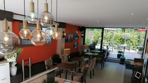 A modern restaurant interior with a central counter, multiple tables, and hanging pendant lights. - Hôtel Miramar Cap d'Antibes (Antibes)