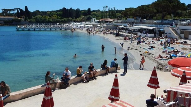 A beach with clear blue water, people sunbathing, and umbrellas. - Hôtel Miramar Cap d'Antibes (Antibes)