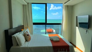 Habitación de hotel con cama, televisor, escritorio y teléfono, y vista al océano.