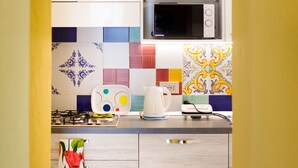 A kitchen with white cabinets, a microwave, a colorful backsplash, and a tiled floor. - Relais Il Sogno di Positano (Positano)