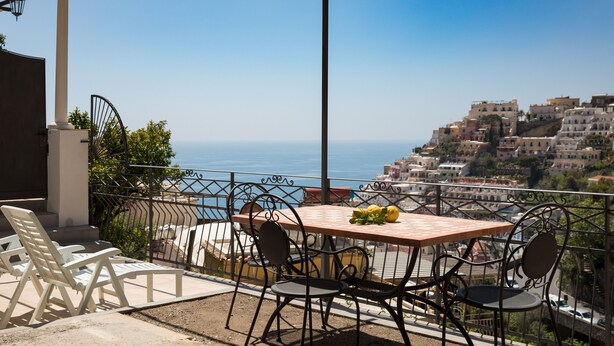 A terrace with a table and chairs overlooking a coastal town. - Relais Il Sogno di Positano (Positano)