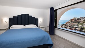 A bedroom with a bed, a nightstand, a window with a view of a coastal town. - Relais Il Sogno di Positano (Positano)