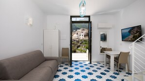 A modern room with a beige sofa, a dining table with chairs, a TV, and a view of a coastal town through a glass door. - Relais Il Sogno di Positano (Positano)