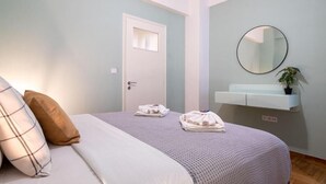 Een slaapkamer met een bed, kussens, een nachtkastje, een spiegel en een wandplank met een plant.