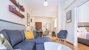 Een moderne woonkamer met een grijze hoekbank, een witte salontafel en een eethoek op de achtergrond.