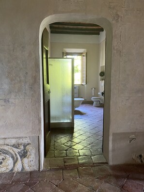 Ein schmaler Flur mit Fliesenboden, der zu einem Badezimmer mit Toilette und Fenster führt.