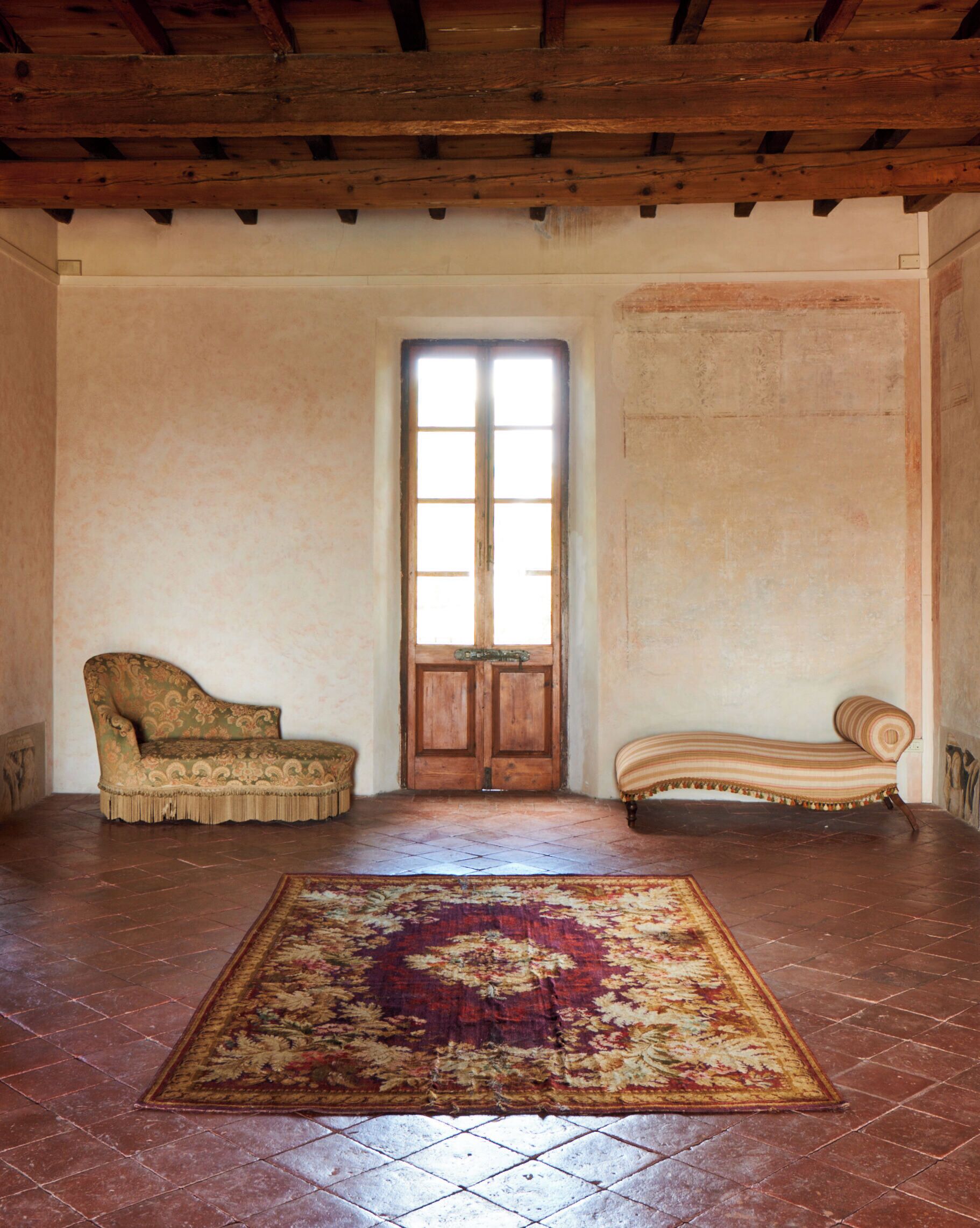 A room with a large wooden door, two upholstered sofas, and a patterned rug on a tiled floor.