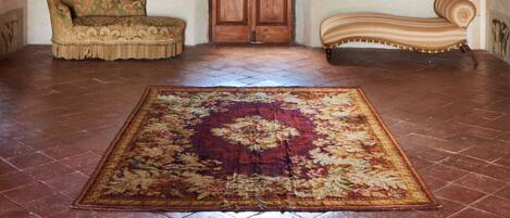 A room with a large wooden door, two upholstered sofas, and a patterned rug on a tiled floor.