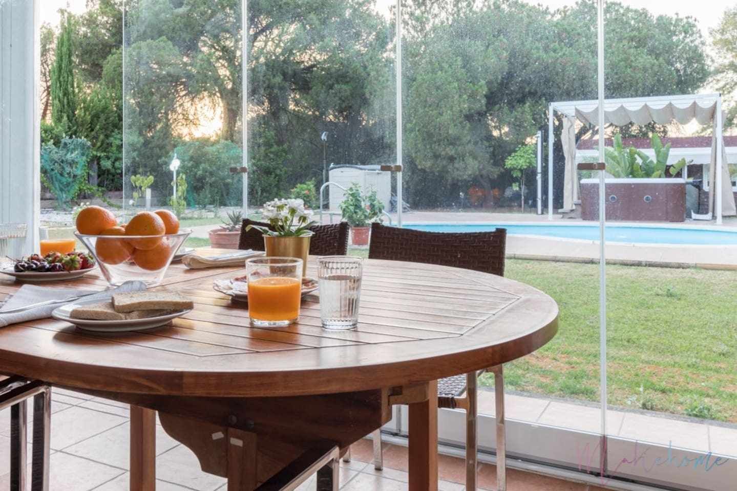 Una mesa redonda de madera con alimentos para el desayuno, un vaso de jugo de naranja y un vaso de agua.