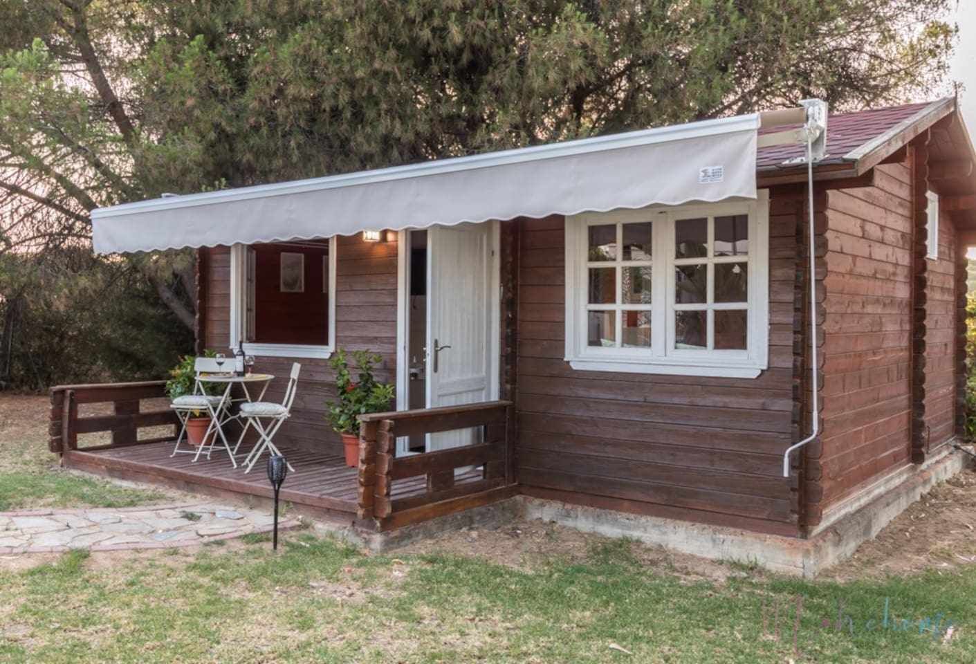 A wooden cabin with a covered porch, a dining table, and chairs.