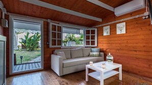 Una stanza accogliente con soffitto in legno, un divano grigio, un tavolo bianco e un'ampia finestra che si affaccia sul verde.