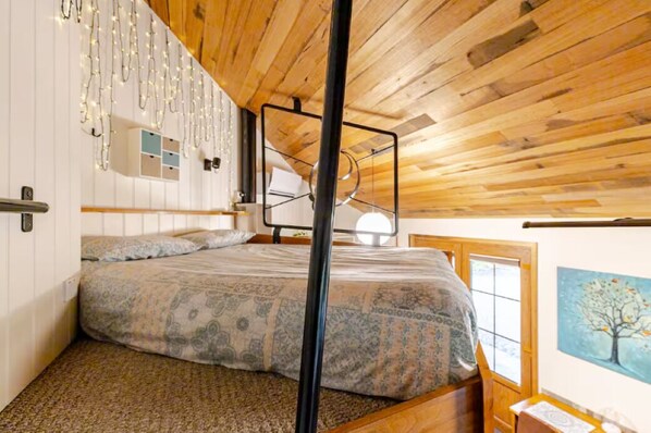 Une chambre avec un plafond en bois, un lit superposé, une étagère fixée au mur et un tableau représentant un arbre.