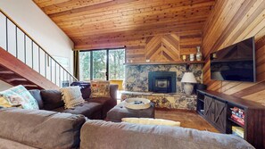 A cozy living room with a stone fireplace, a television mounted on the wall, and a wooden ceiling.