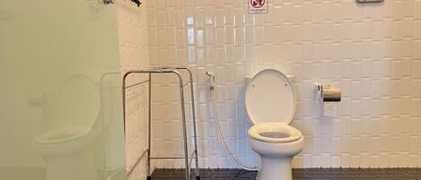 Un baño con inodoro blanco, barandilla, letrero de prohibición de basura y pared con azulejos.