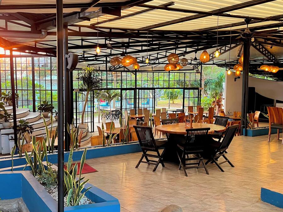 An indoor dining area with tables and chairs, large windows, and hanging lights.