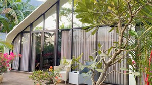 A modern outdoor space with a glass enclosure, wicker furniture, and potted plants. - Lucca Resort & Residence (Bandengan)