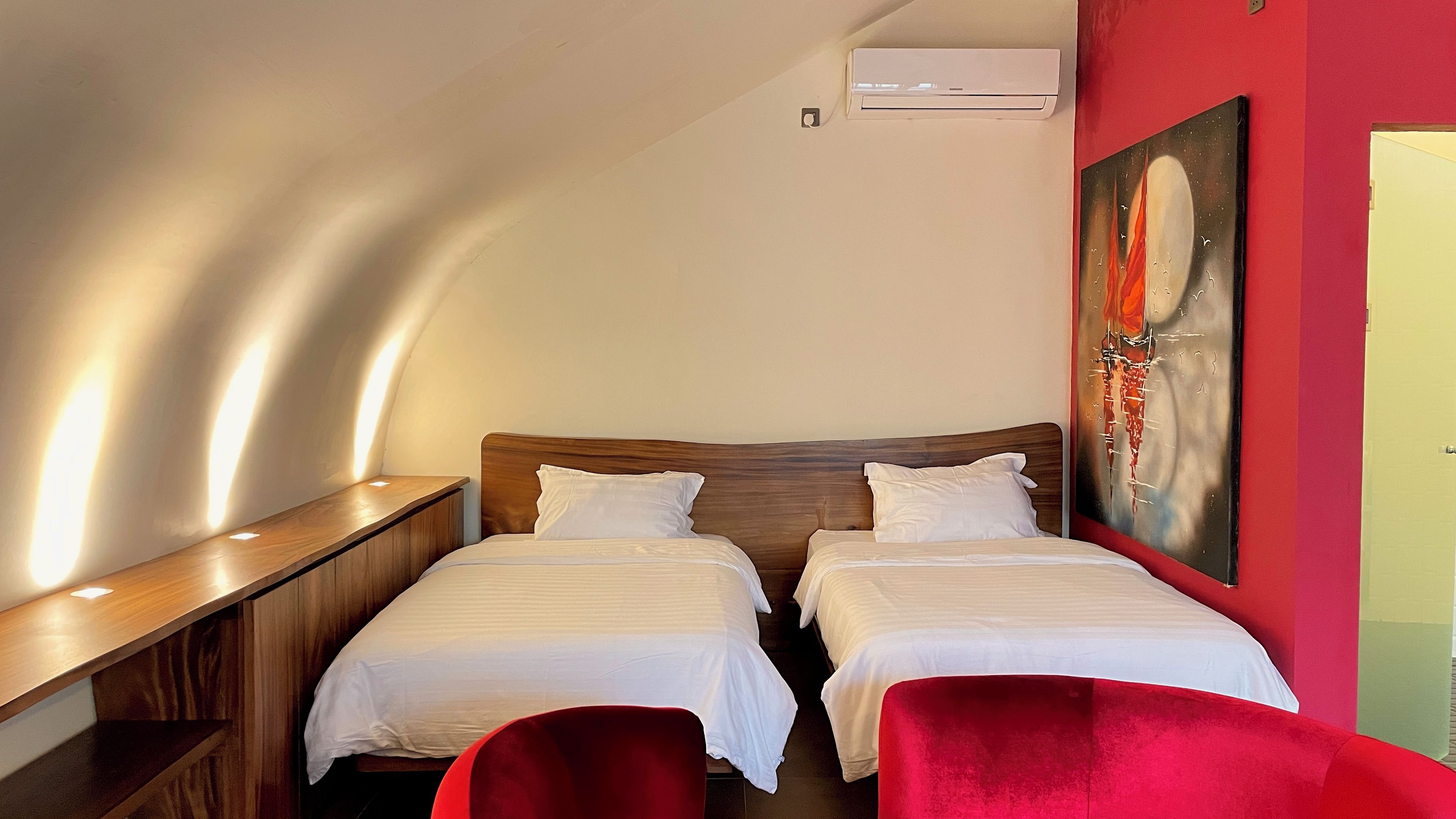 A hotel room with two beds, a red chair, a painting on the wall, and a wooden desk.