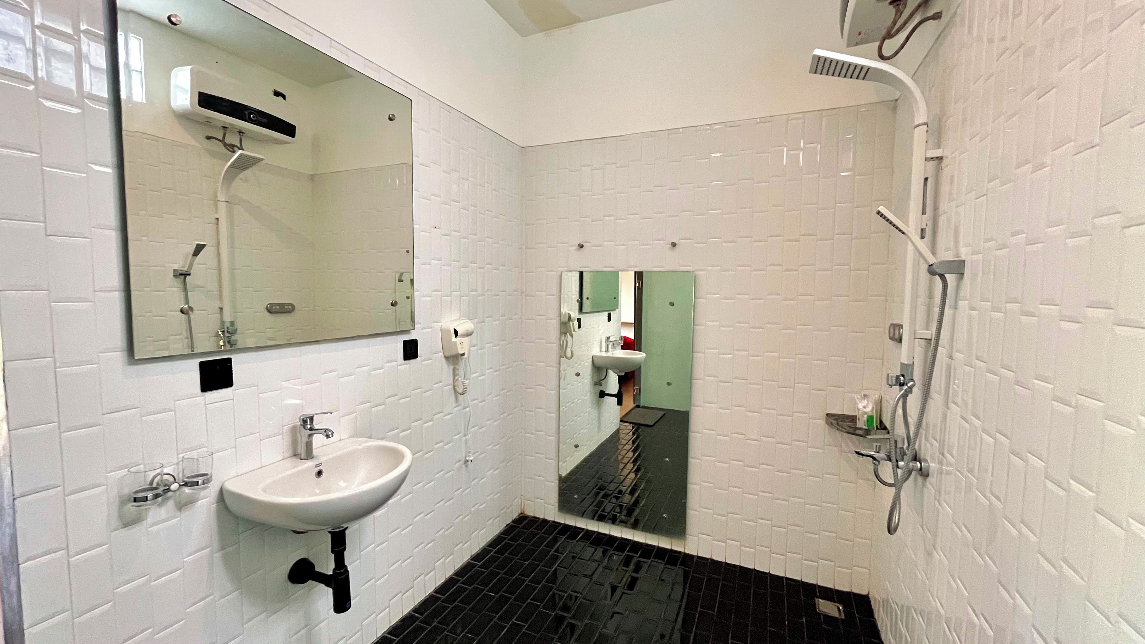 Ein Badezimmer mit weiß gefliesten Wänden, einem weißen Waschbecken, einem Spiegel, einer Dusche und einer grünen Tür.