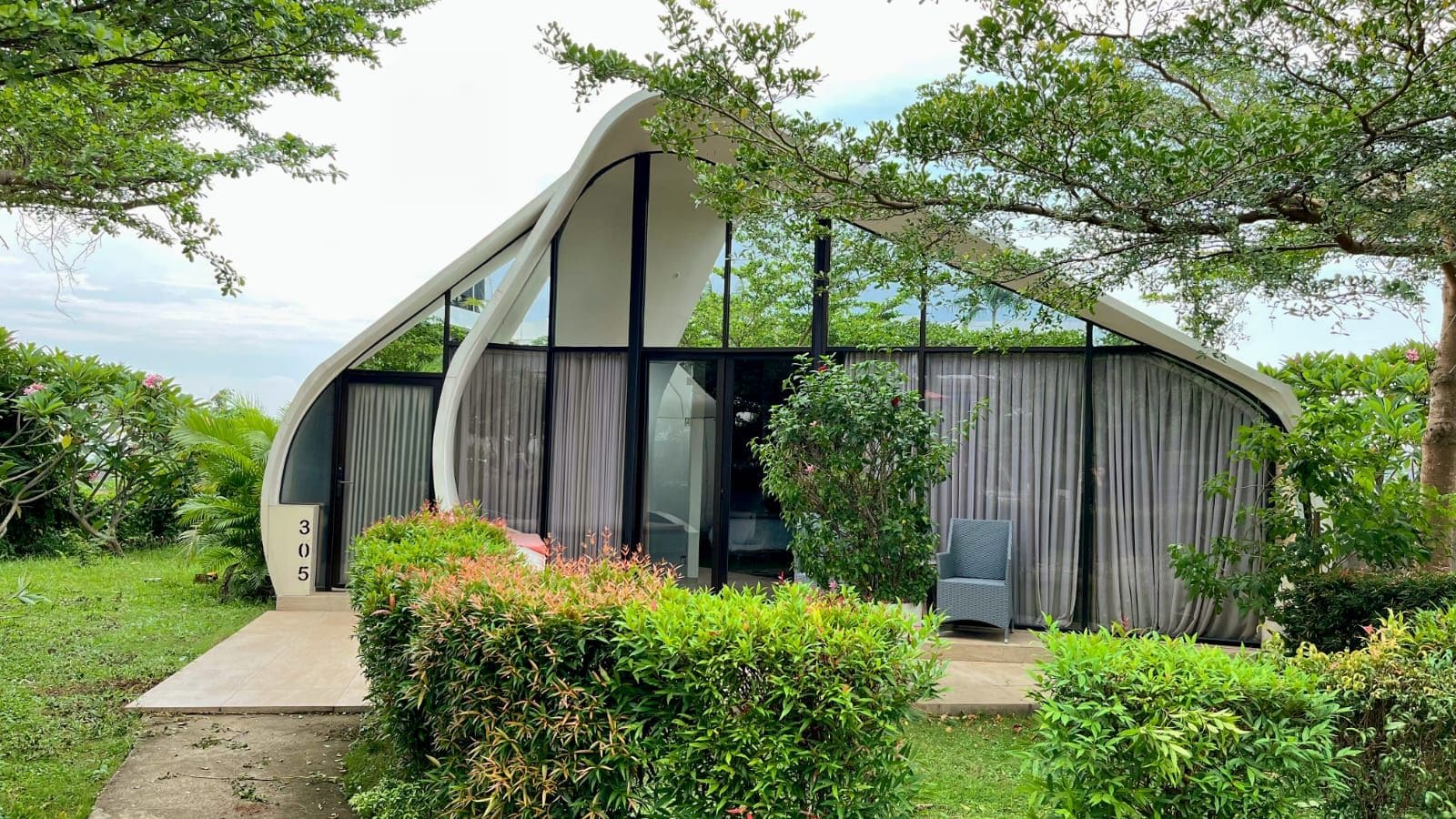 Une maison moderne au design épuré, avec un chemin menant à l’entrée et une végétation luxuriante qui entoure la propriété.
