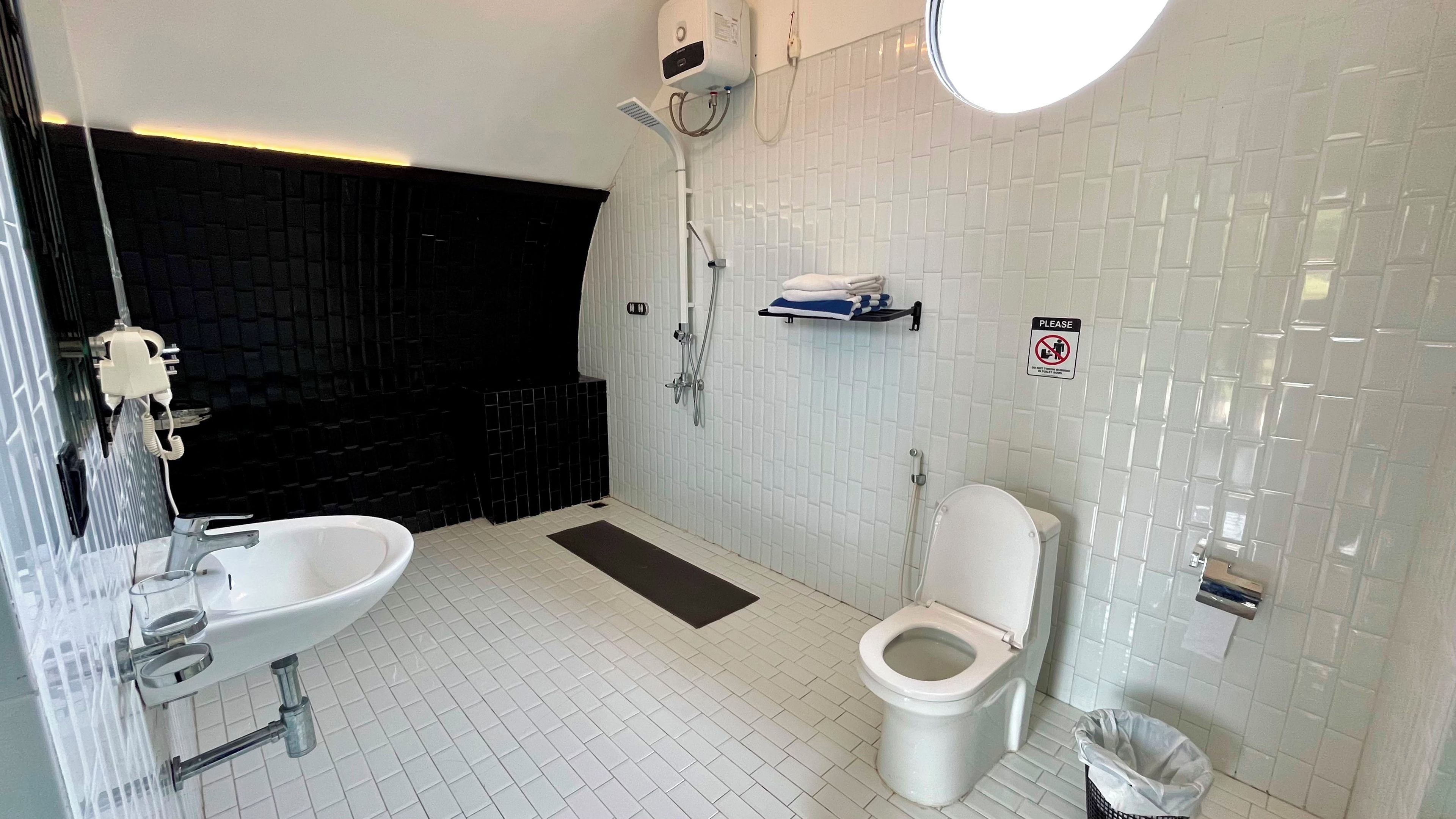 A modern bathroom with a white sink, toilet, and shower. There is a black tiled wall and a sign indicating no smoking.