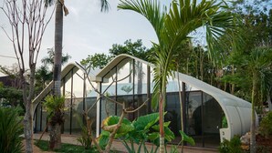 Un edificio moderno con techo curvo y amplias ventanas de vidrio, rodeado de vegetación tropical.