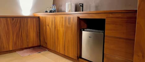 A kitchen with wooden cabinets, a stainless steel refrigerator, and a countertop with bottles and a kettle.