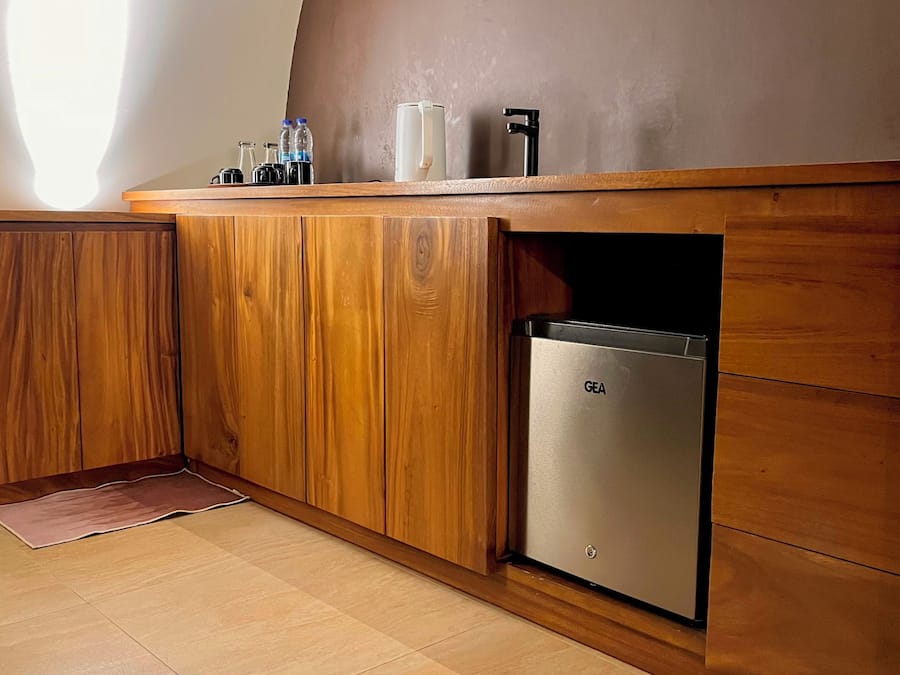 Une cuisine avec des meubles de rangement en bois, un réfrigérateur en acier inoxydable et un plan de travail orné de bouteilles et d’une bouilloire.
