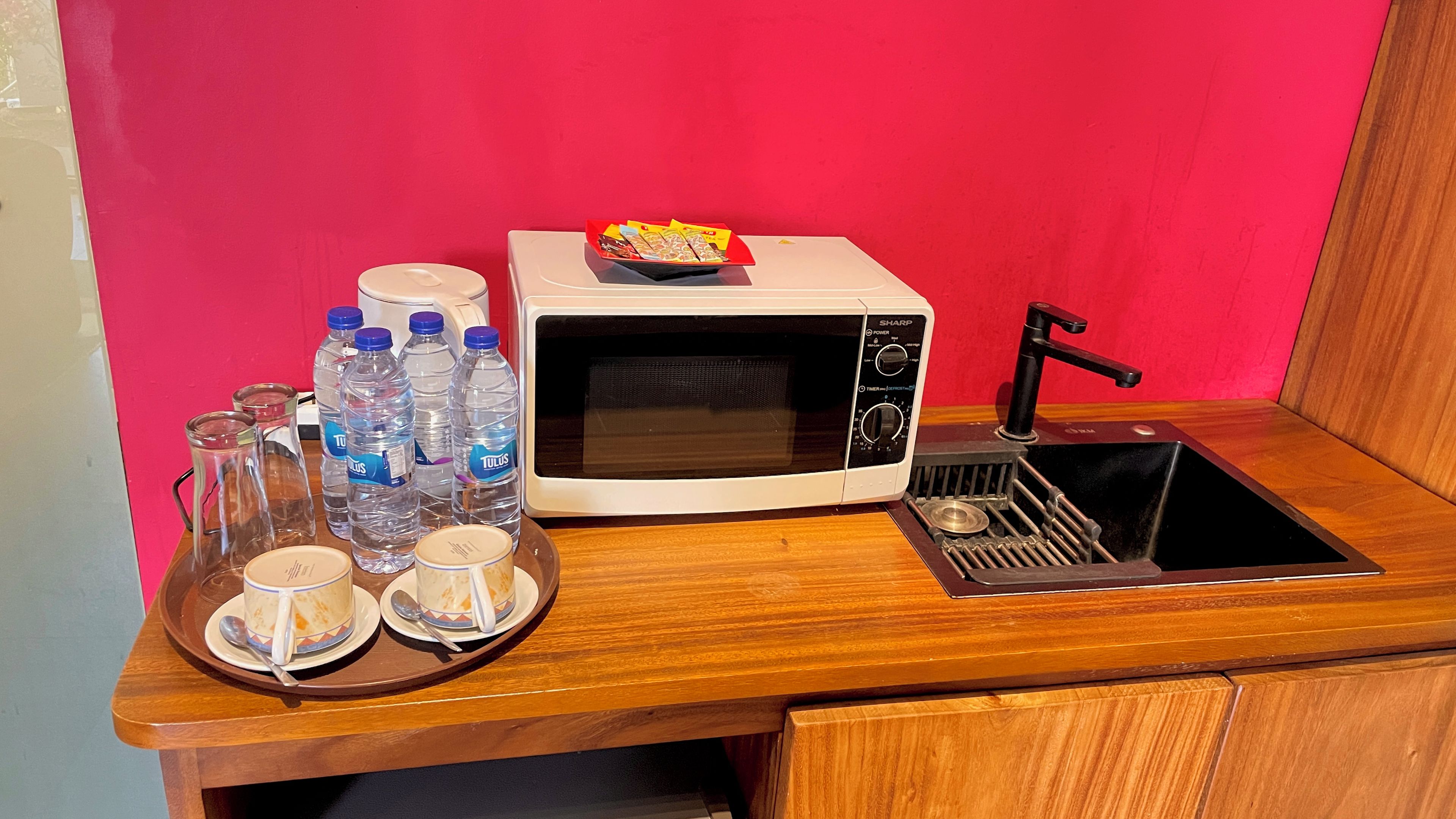 A kitchen with a microwave, sink, and a tray with cups and water bottles.