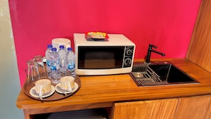 Una cocina equipada con microondas, pileta y una bandeja con vasos y botellas de agua.