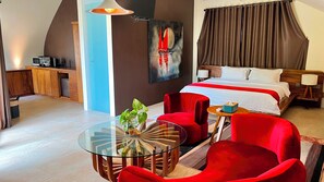 A modern hotel room with a bed, red chairs, a glass table, and a painting on the wall. - Lucca Resort & Residence (Bandengan)