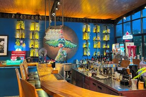 A bar area with a long counter, shelves with bottles, and a mural on the wall. - Lucca Resort & Residence (Bandengan)
