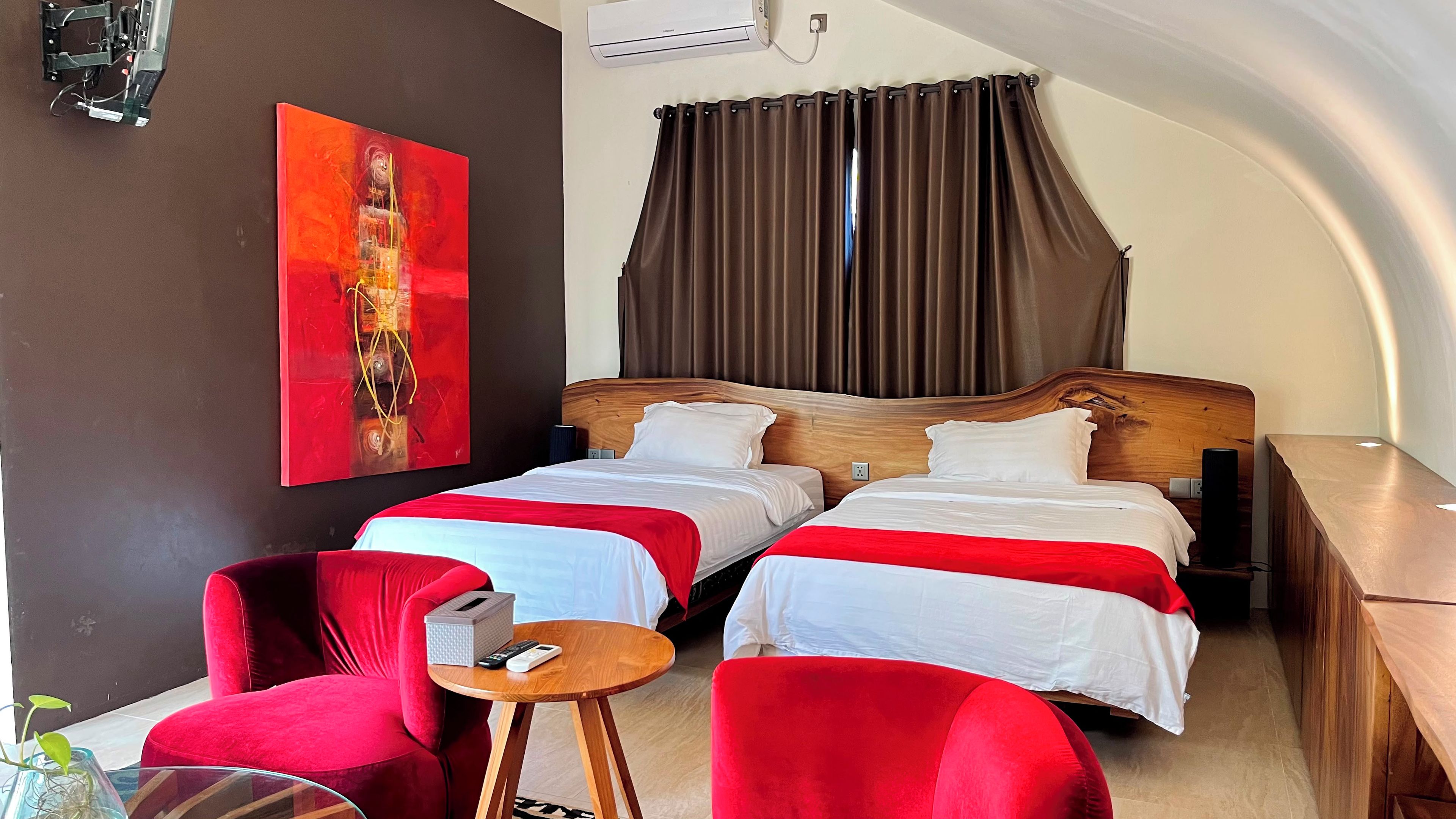 Ein Hotelzimmer mit zwei Betten, einem roten Sessel, einem kleinen Tisch und einem Gemälde an der Wand.