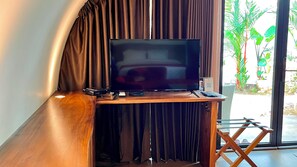 A television on a wooden stand with a remote control, a phone, and a QR code sign. - Lucca Resort & Residence (Bandengan)