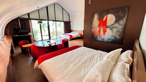A hotel room with a large bed, a desk, a red chair, and a painting on the wall. - Lucca Resort & Residence (Bandengan)