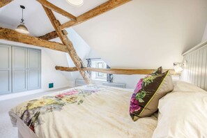 A bedroom with exposed wooden beams, a bed with floral bedding, and a window with a view of the outside.